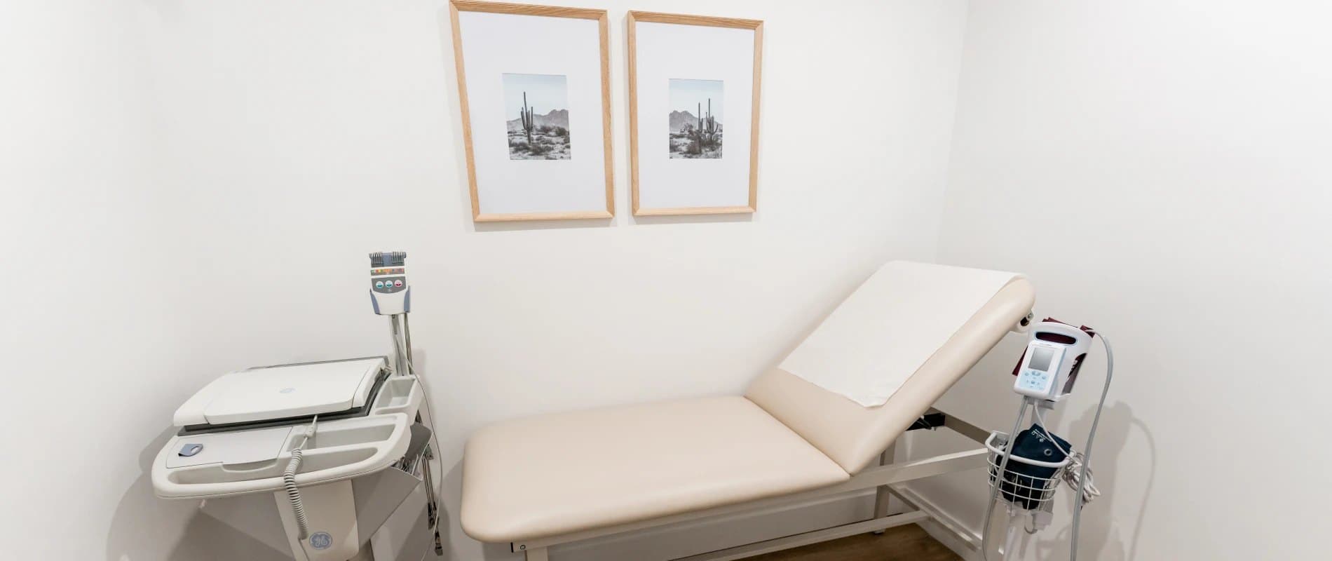 Exam room with an exam table, blood pressure monitor and framed prints